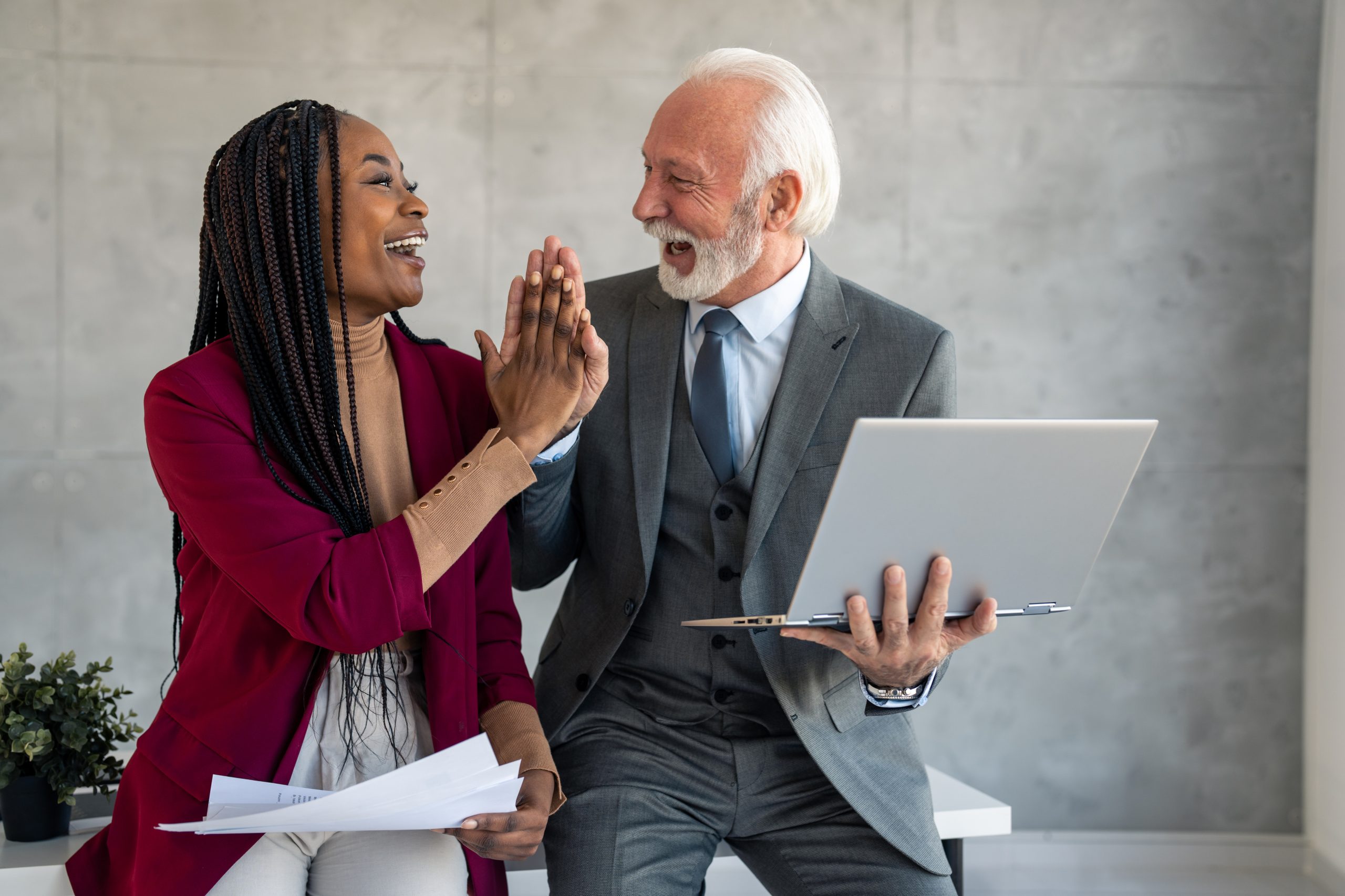 Senior business man and pretty young business woman high fiving in office Two satisfied diverse professionals coworkers senior business man and cheerful business woman high fiving in office celebrating success, good cooperation result, partnership teamwork and motivation in office.